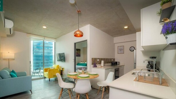 A modern kitchen with white countertops, a dining area with a round table and white chairs, and a living area with a sofa and a coffee table.