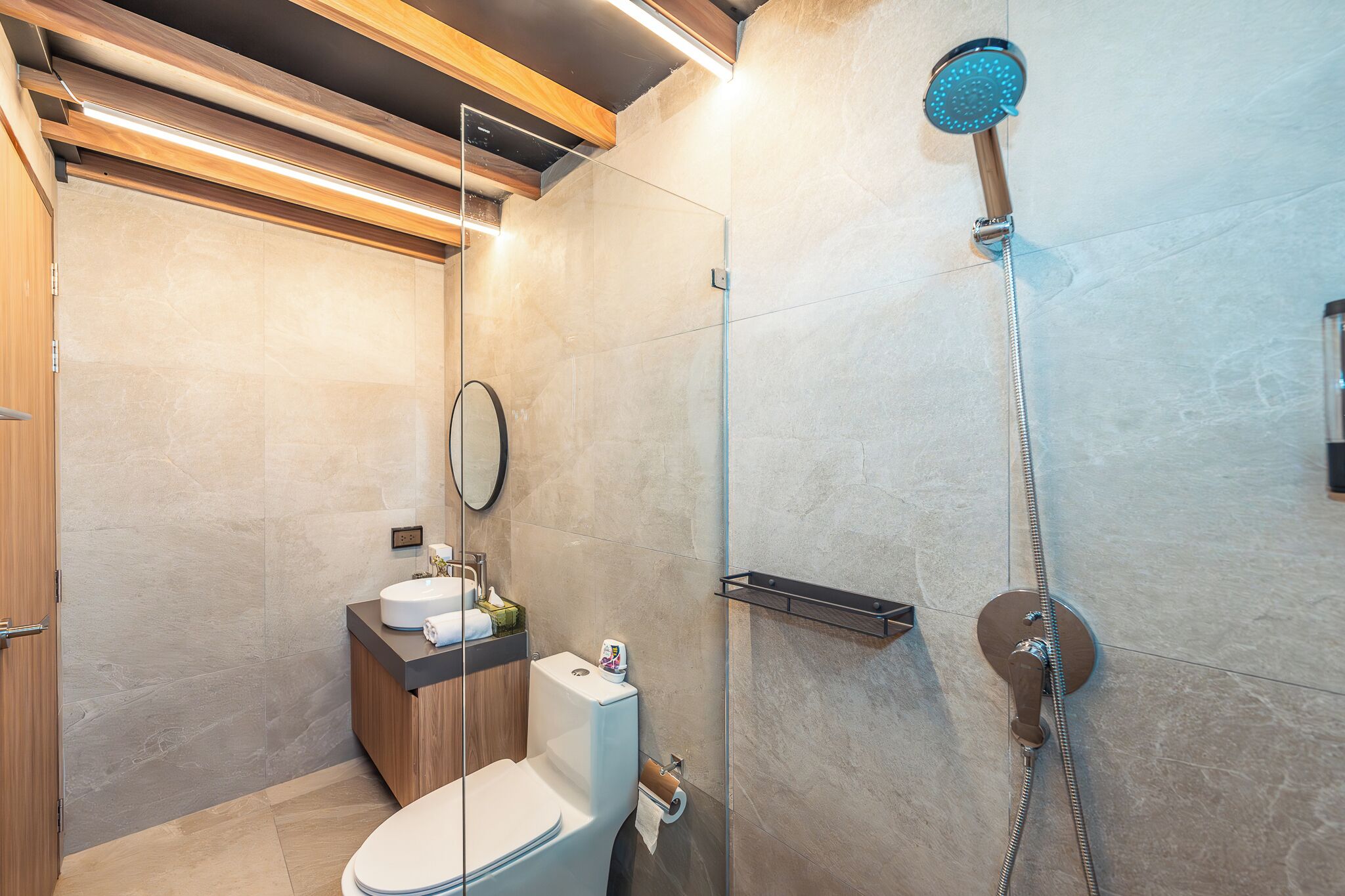 Un baño moderno con cabina de ducha de vidrio, inodoro y lavamanos con encimera de madera.