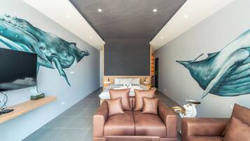 A modern hotel room with a large mural of a whale on the walls, a sofa, a TV, and a bedside table with a lamp.