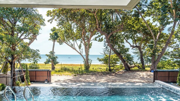 An outdoor swimming pool with a view of the ocean, surrounded by trees and a sandy area. - Merbrisa Rayong - Ao khai beachfront (Klaeng)