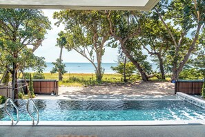 An outdoor swimming pool with a view of the ocean, surrounded by trees and a sandy area.