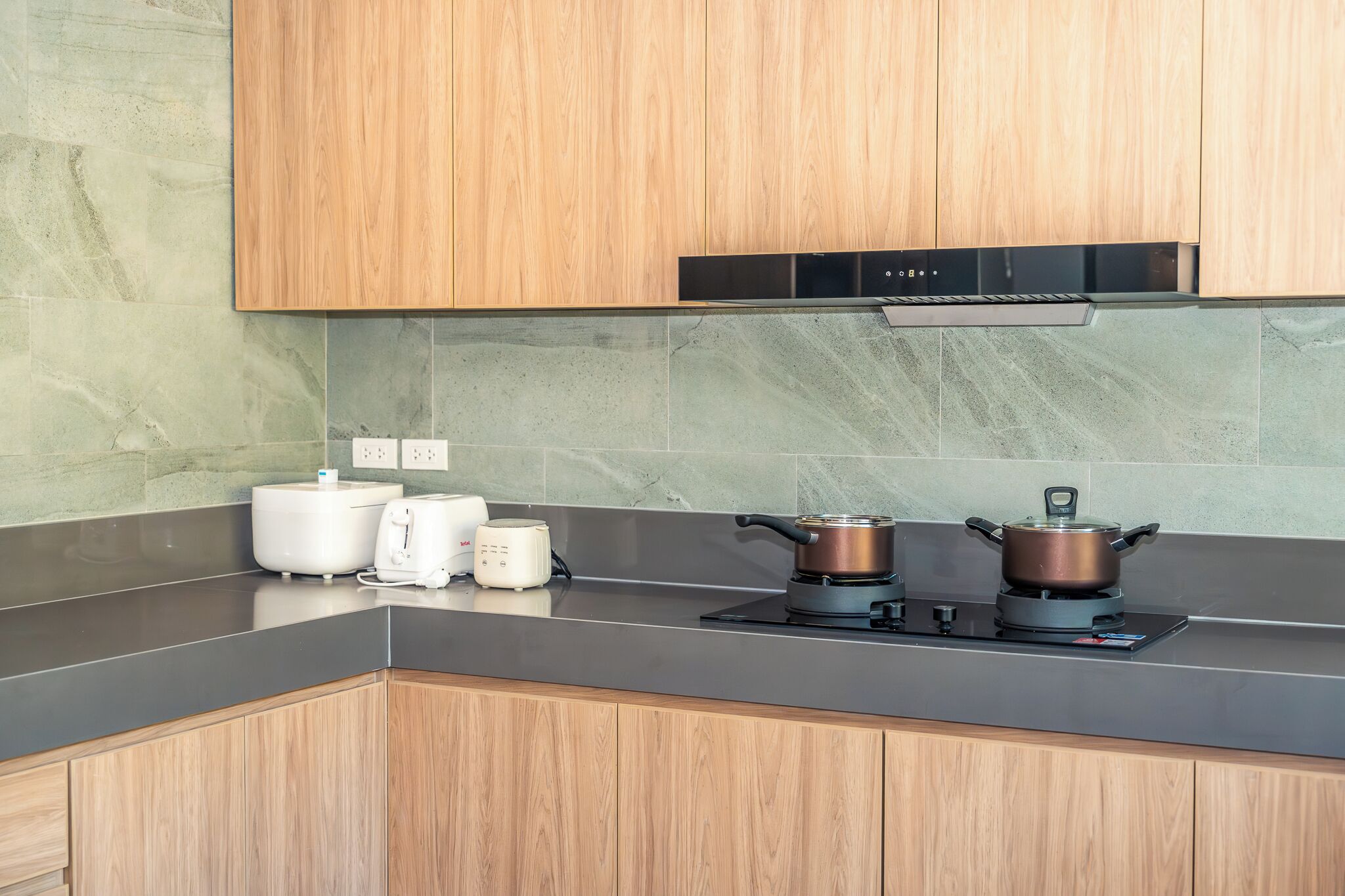 A modern kitchen with wooden cabinets, a black range hood, a gas stove, a kettle, and a toaster.