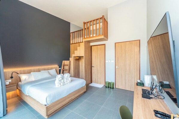A modern hotel room with a wooden bed, a desk with a computer, and a balcony.