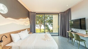 A modern bedroom with a large bed, a desk with a TV, and a view of trees through the window. - Merbrisa Rayong - Ao khai beachfront (Klaeng)
