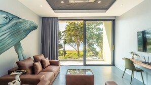 A modern living room with a large window, a sofa, a coffee table, and a desk with a chair. - Merbrisa Rayong - Ao khai beachfront (Klaeng)