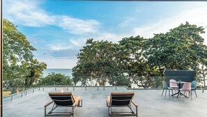 A terrace with two lounge chairs and a table, overlooking a scenic view of the sea and trees. - Merbrisa Rayong - Ao khai beachfront (Klaeng)