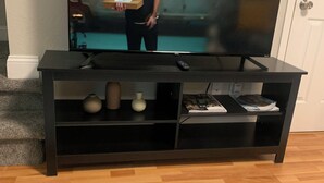 A television on a black stand with a remote control, a vase, and a small plant. - Welcome to our Place (Charlotte)