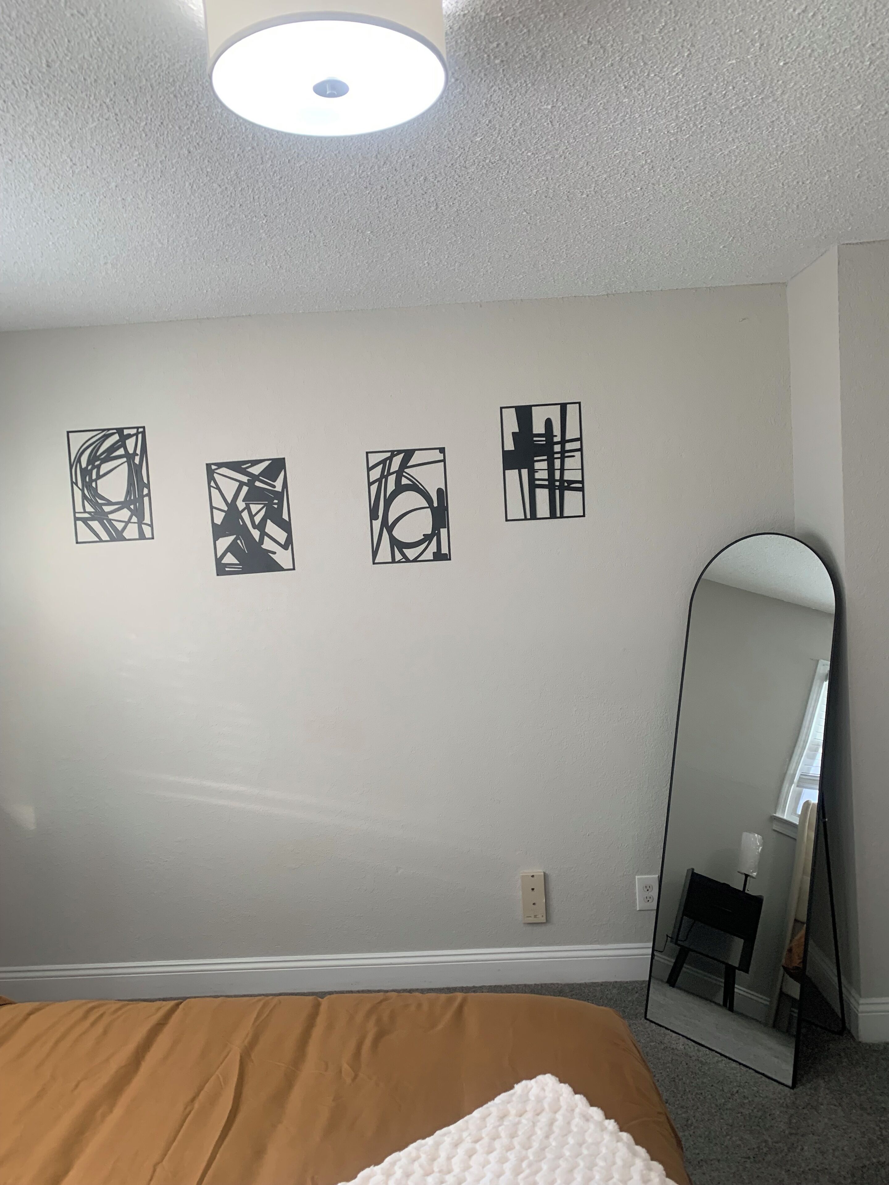 Une chambre à coucher comprenant un lit, un grand miroir et quatre œuvres d’art abstraites accrochées au mur.