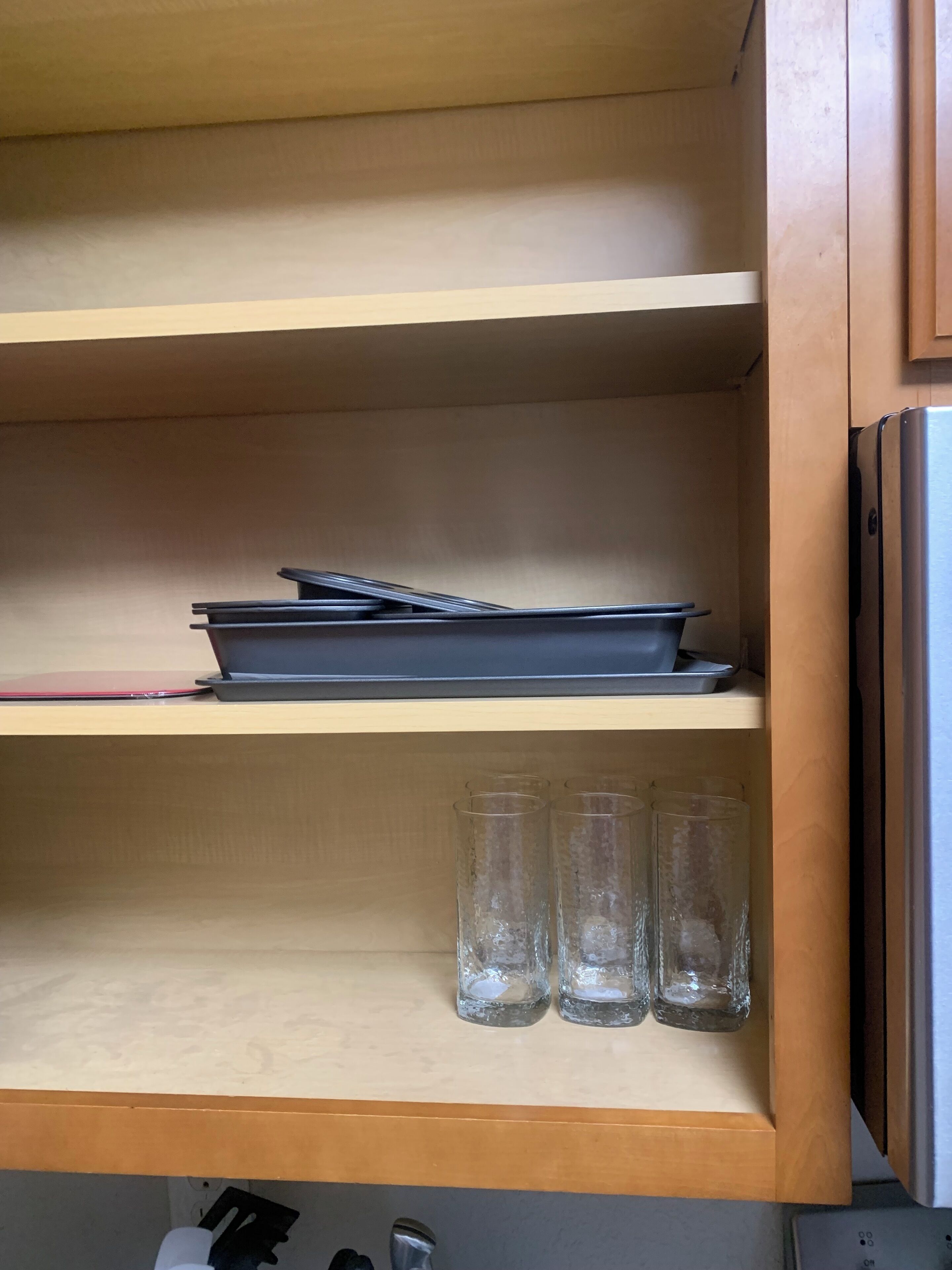 A kitchen with wooden shelves, a laptop, a red notebook, and four clear glasses.