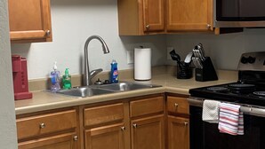 A kitchen with wooden cabinets, a stainless steel sink, a stove, and a microwave. - Welcome to our Place (Charlotte)