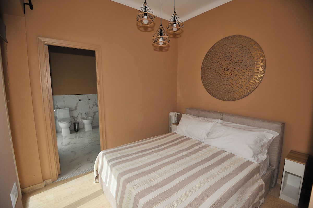 A bedroom with a bed, a round wall decoration, and a bathroom visible through an open door.