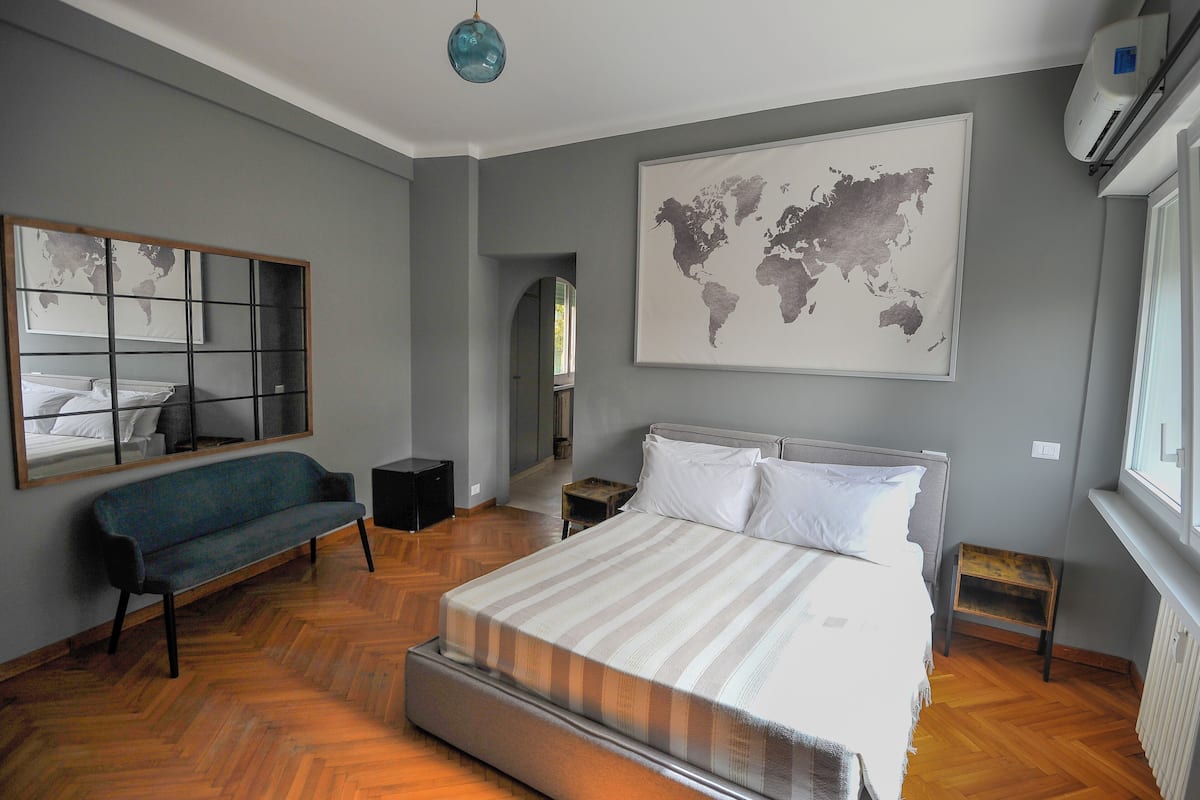 A modern bedroom with a large bed, a bench, a world map, and a window.