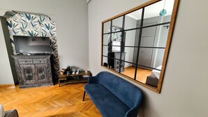 A living room with a blue sofa, a wooden coffee table, a fireplace with a patterned curtain, and a large mirror on the wall. - Boutique Suite Valadier (Rome)