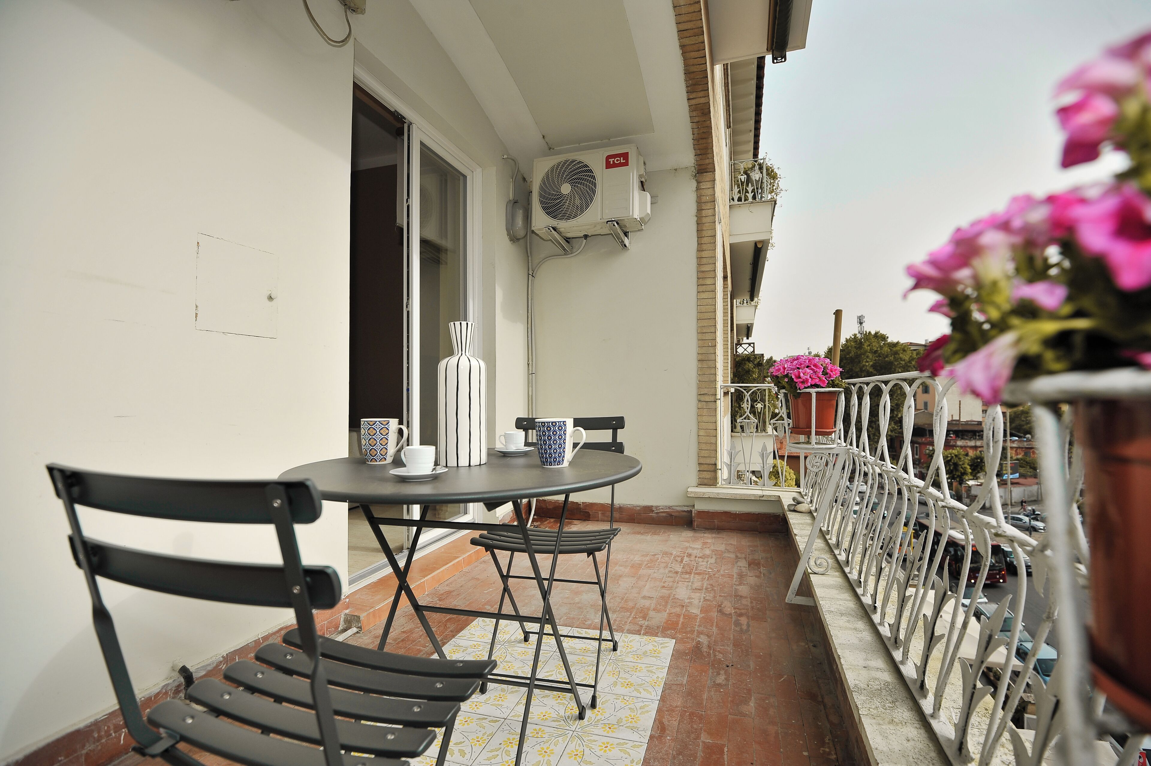 An outdoor balcony with a table and chairs, an air conditioning unit, and potted plants.
