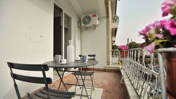 An outdoor balcony with a table and chairs, an air conditioning unit, and potted plants.