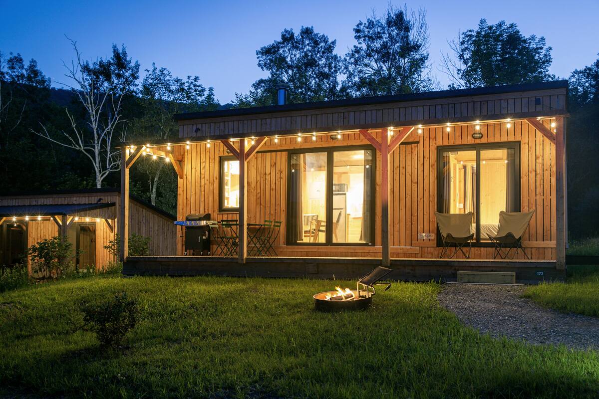 A wooden cabin with a covered patio, a grill, and a fire pit.