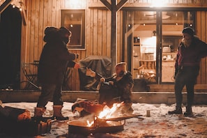 Un grupo de personas reunidas alrededor de una fogata en una cabaña de madera, con el suelo cubierto de nieve.