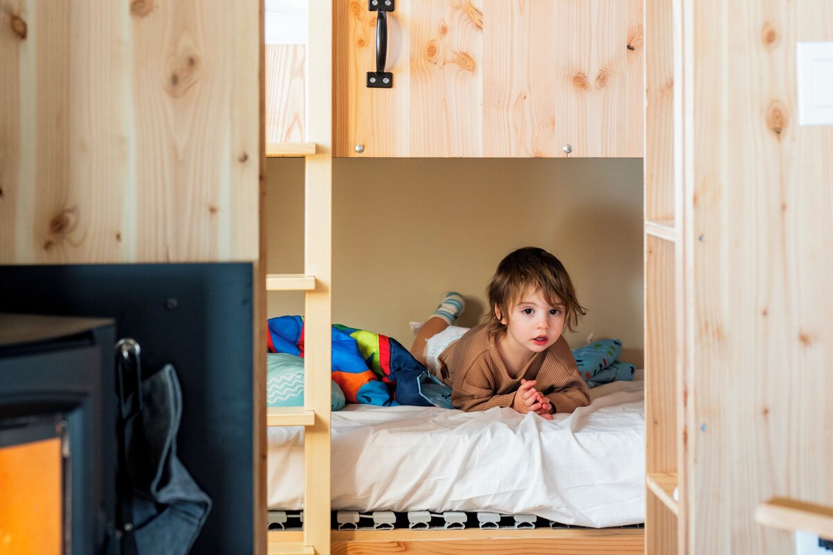 Habitación con literas de madera, un radiador visible, literas infantiles y una litera inferior con una manta colorida.