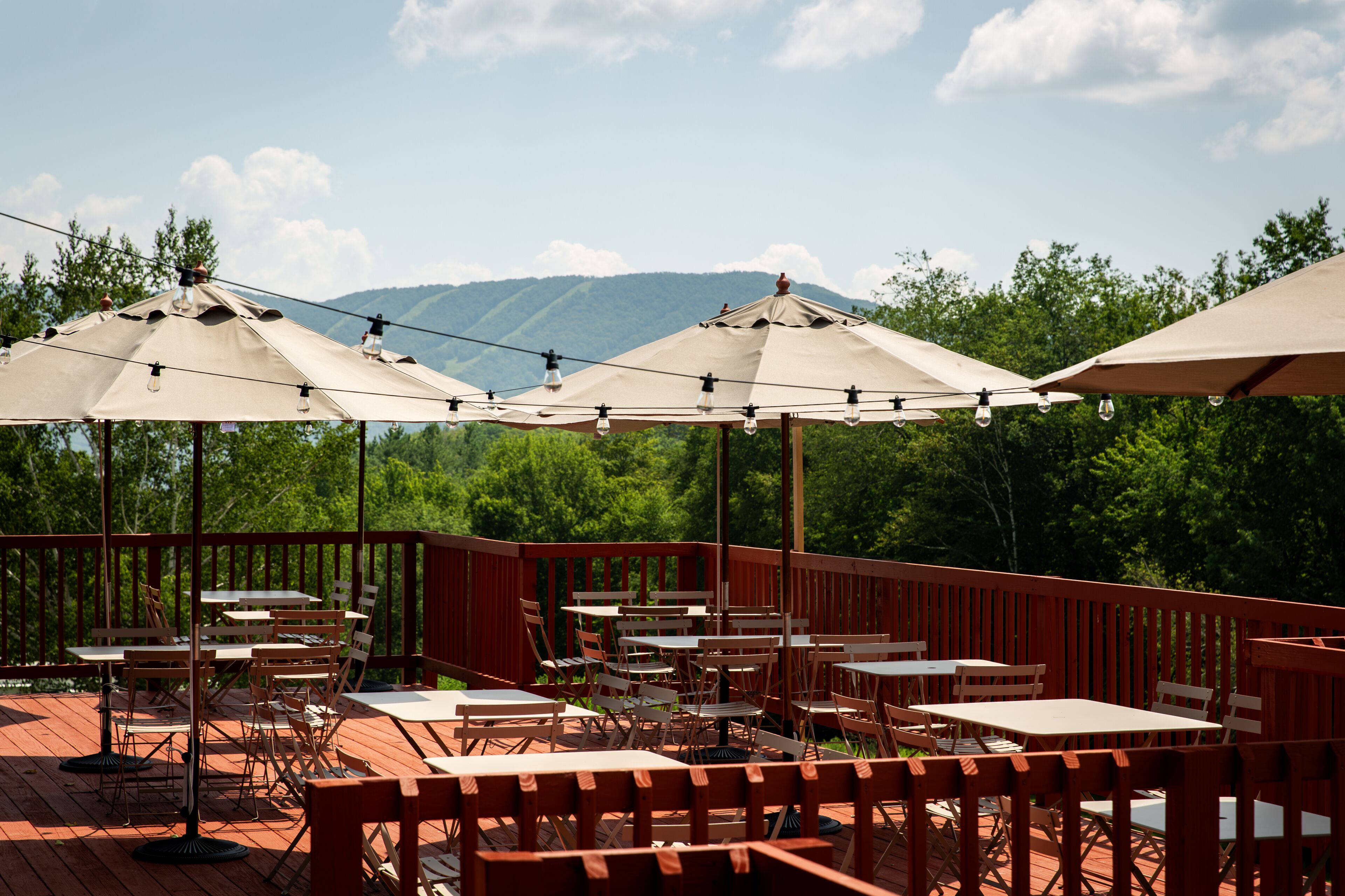 An outdoor patio with tables and chairs, string lights, and umbrellas.