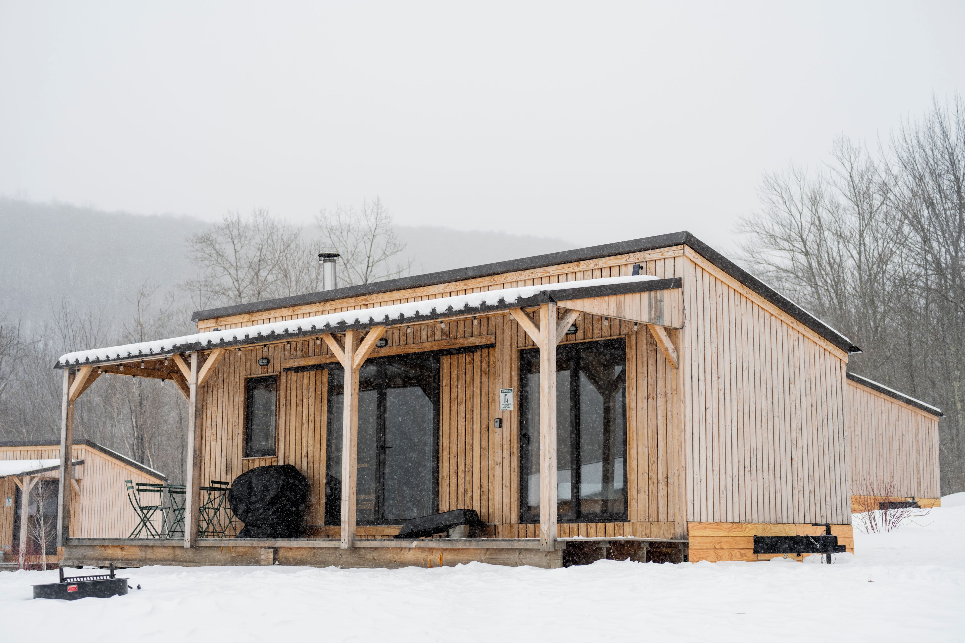 A wooden cabin with a covered porch, large windows, and a snow-covered roof.