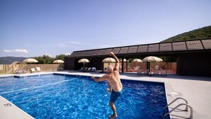 A swimming pool with a wooden deck, lounge chairs, and umbrellas. - Huttopia Berkshires  (Williamstown)
