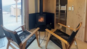 A cozy room with a wood-burning stove, two wooden chairs, a small table, and a window overlooking a snowy landscape. - Huttopia Berkshires  (Williamstown)