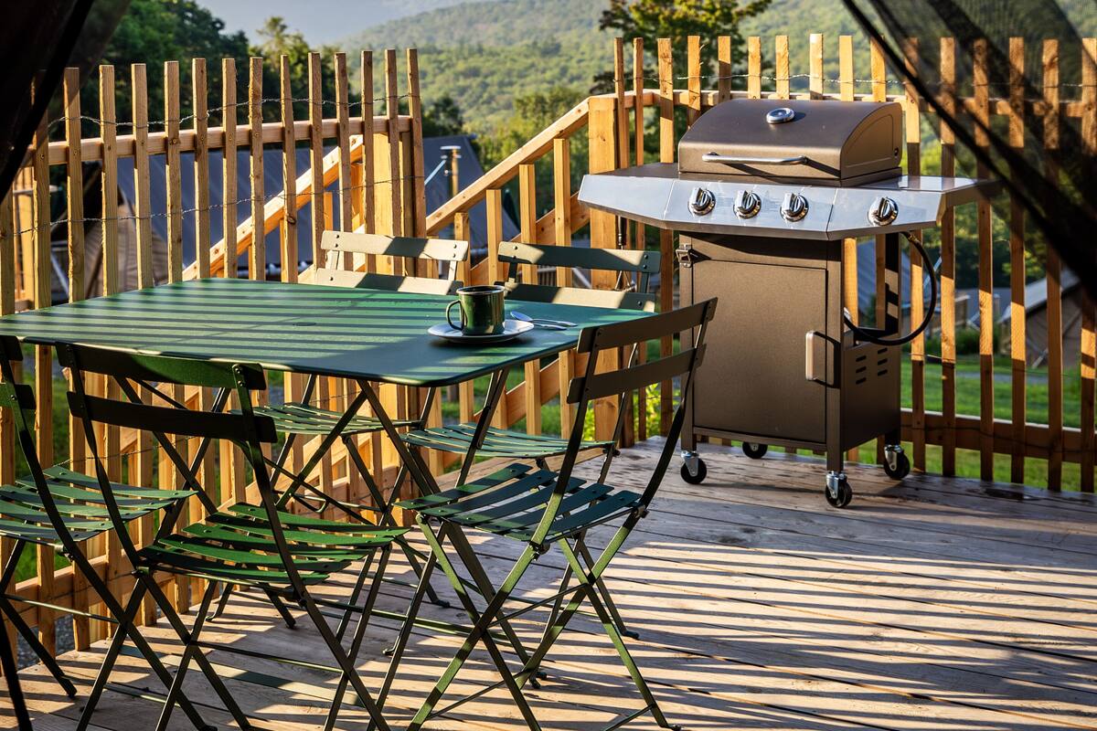 A wooden deck with a table and chairs, a grill, and a view of the mountains.