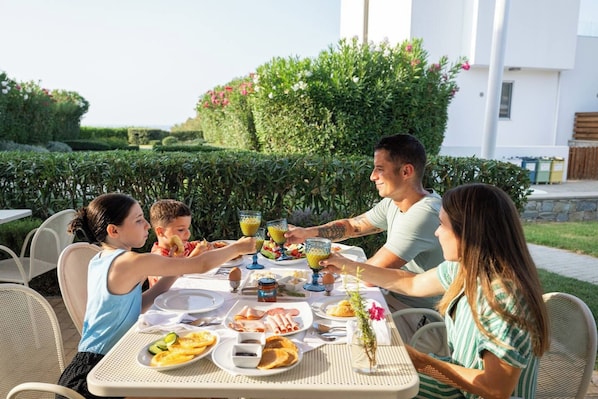 Un grupo de personas cenando al aire libre en una mesa con diversos platos y bebidas.