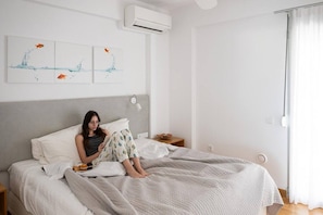 Een slaapkamer met een bed, nachtkastje, een wandairconditioner en een raam met gordijnen.