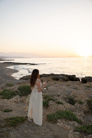 A woman standing on a rocky beach with the ocean in the background.