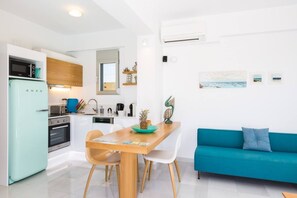 Cocina funcional con refrigerador, horno y microondas. Se observa una mesa de comedor con sillas y un sofá azul.