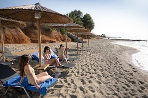 Een strand met ligbedden en rieten parasols.