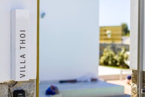 Een wit bord met de tekst 'VILLA THOI', bevestigd aan een stenen constructie.