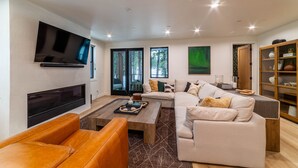 Ein modernes Wohnzimmer mit großem Flachbildfernseher, einem Ecksofa, einem Holztisch und einer Glastruhe.