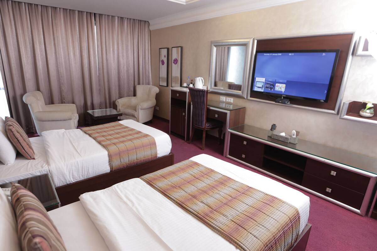 A hotel room with two beds, a desk, a chair, a television, and a minibar.