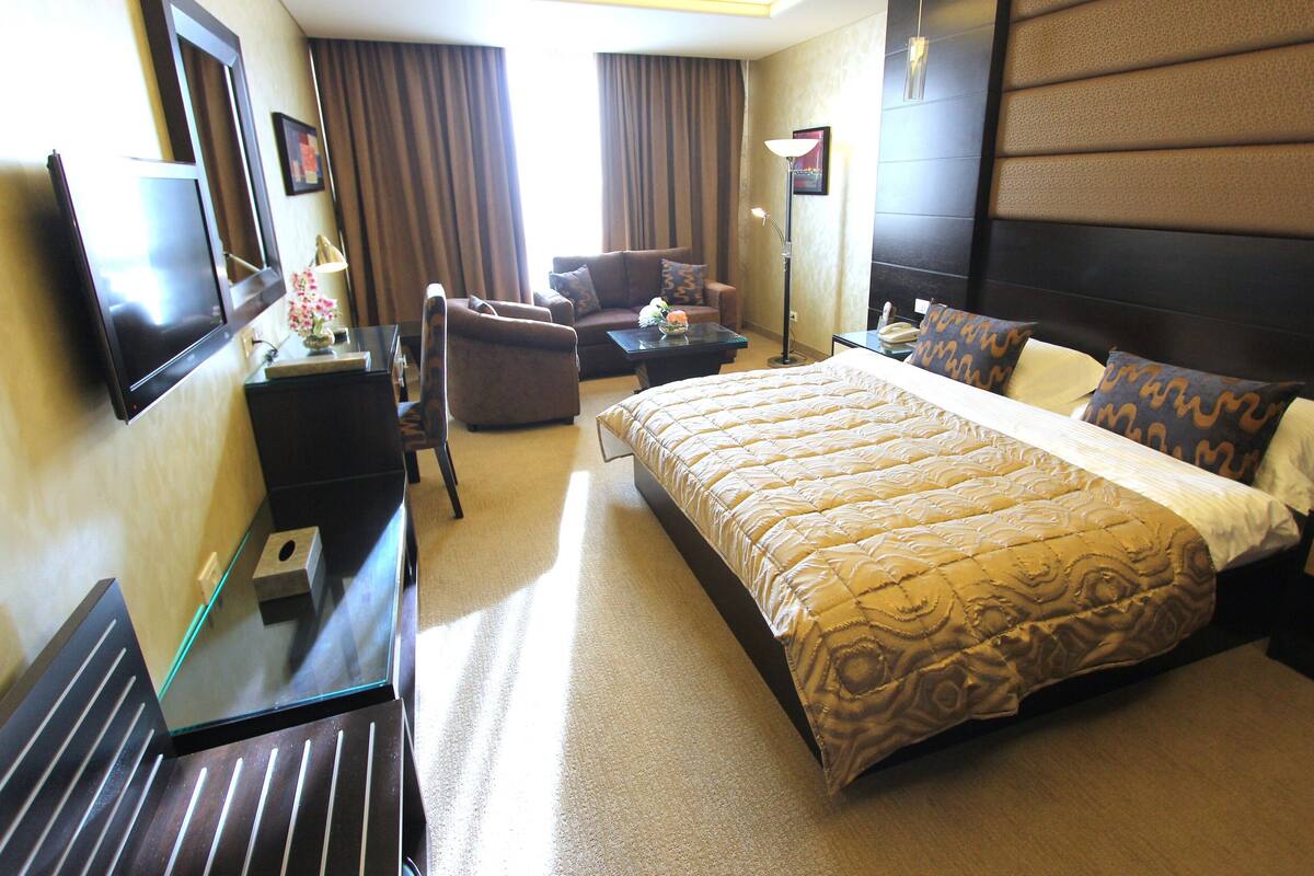 A hotel room with a bed, a desk, a chair, a sofa, and a TV.