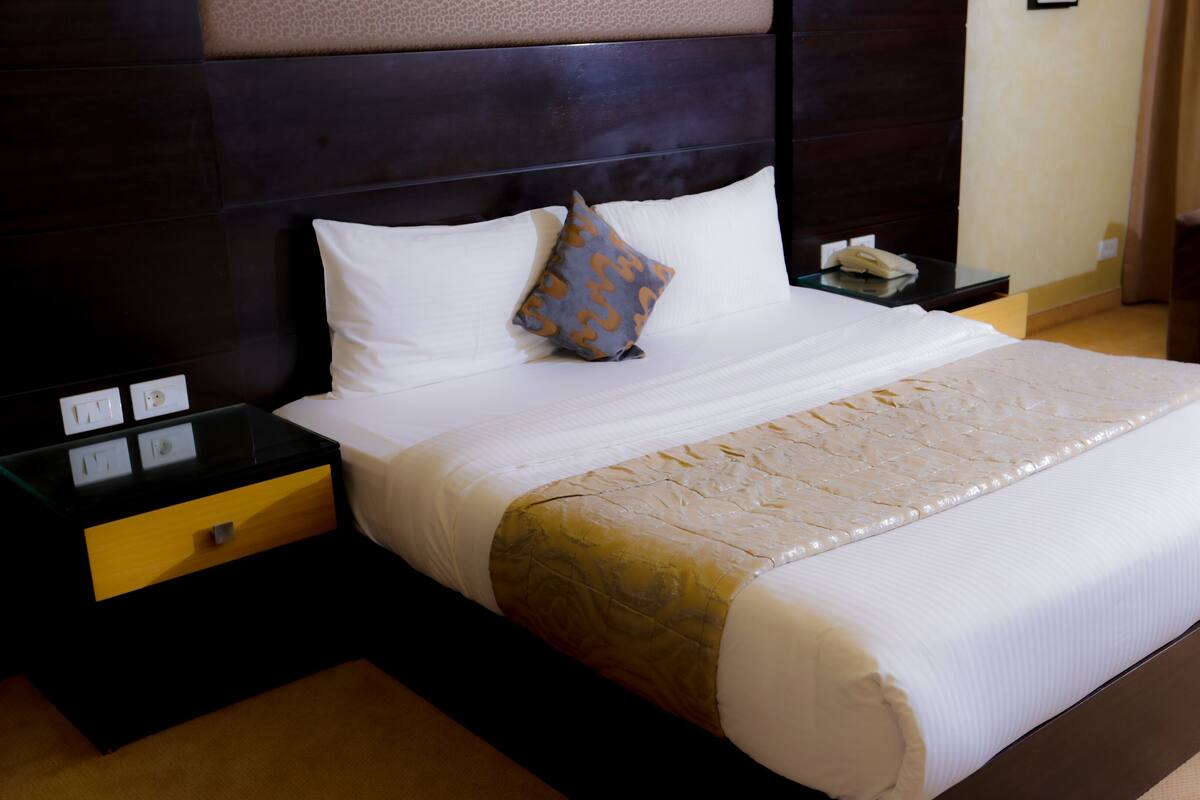 A neatly made bed with white linens, a patterned throw, and a brown headboard.