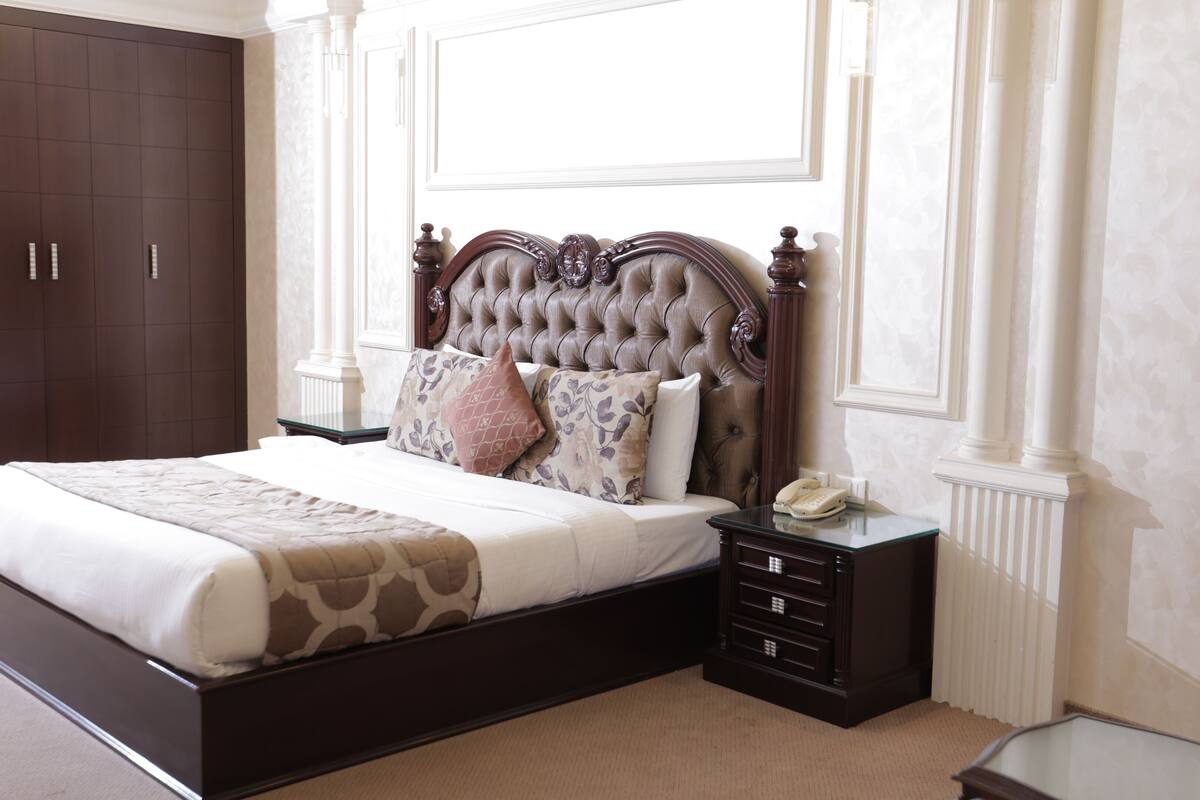 A bedroom with a large bed, a nightstand, a telephone, and a wardrobe.