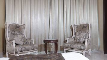 A room with two ornate armchairs, a small round table, and a large bed.
