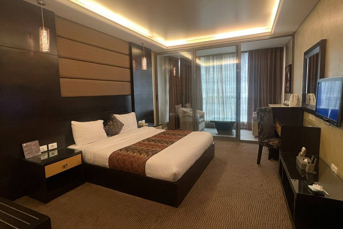 A modern hotel room with a large bed, a desk, a TV, and a seating area with a view of the outdoors.