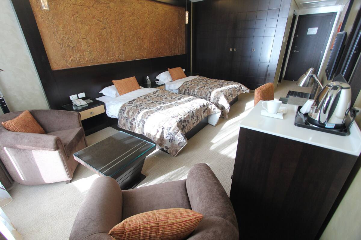 A hotel room with two beds, a sofa, a coffee table, a desk, and a large artwork on the wall.
