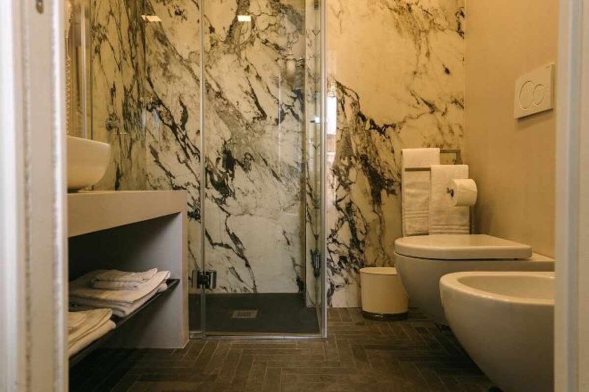 A modern bathroom with a glass shower enclosure, marble walls, a white sink, and a toilet.