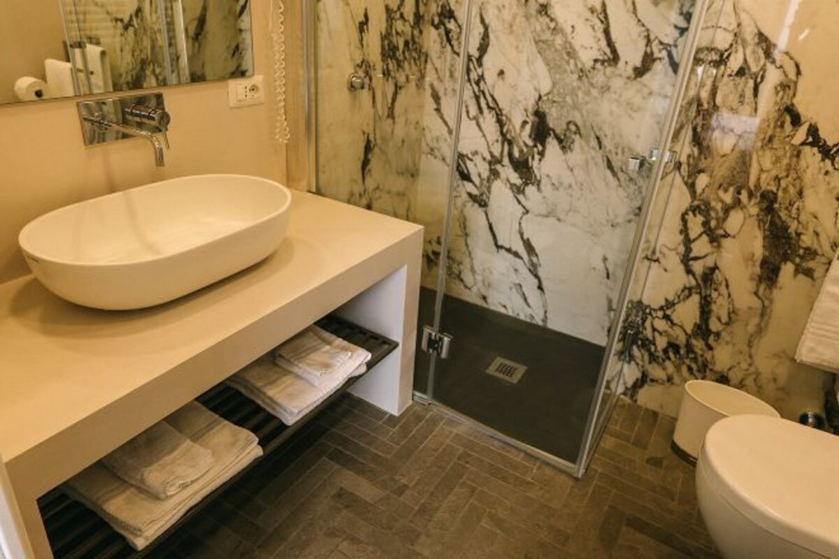 A modern bathroom with a large oval sink, a glass shower enclosure, and a marble backsplash.