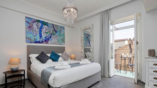 Une chambre avec un grand lit, un lustre, un tableau et une vue sur le balcon.