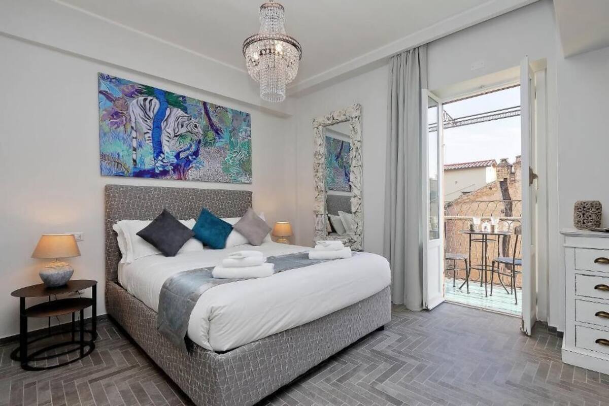 A bedroom with a large bed, a chandelier, a painting, and a balcony view.