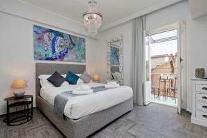 A bedroom with a large bed, a chandelier, a painting, and a balcony view. - Boutique Suites della Croce (Rome)