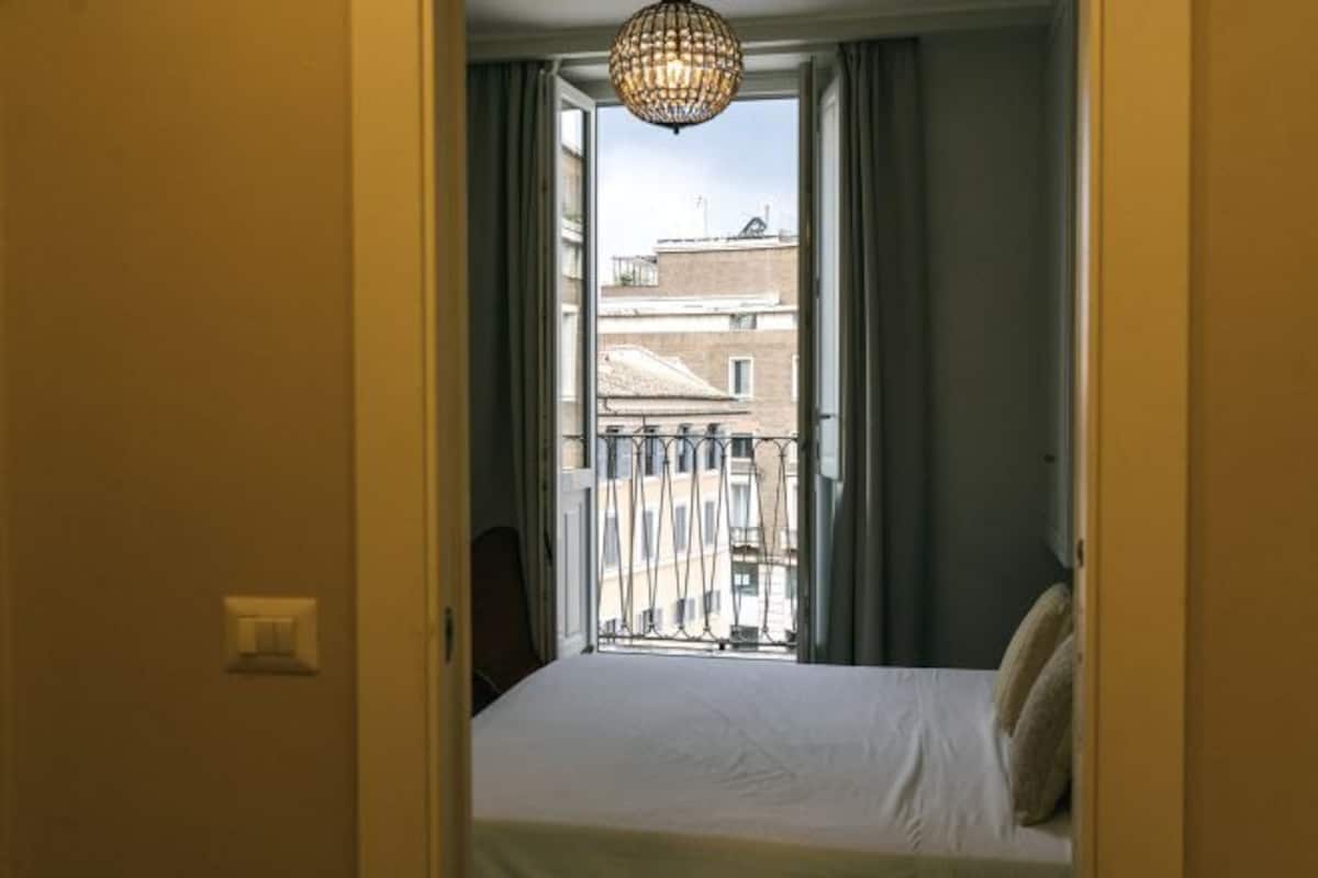 Une chambre d’hôtel avec un lit, un luminaire suspendu et une vue sur les bâtiments par la fenêtre.