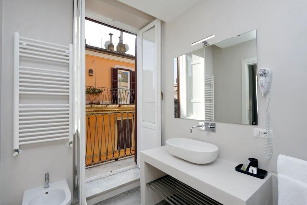 Une salle de bain moderne avec un lavabo blanc, un grand miroir et un sèche-cheveux fixé au mur.