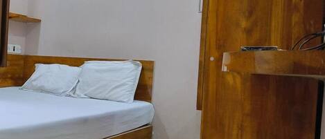 A bed with a wooden headboard and white bedding, a wooden wardrobe, and a small shelf.