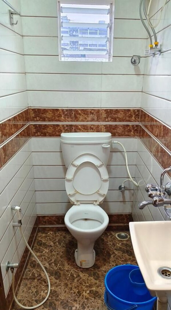A small bathroom with a toilet, a sink, and a window above the toilet. - HOTEL SOCIETY (Kolkata)